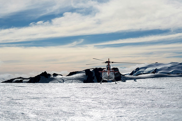Helicopter landing on a snowy mountain under a cloudy sky.
