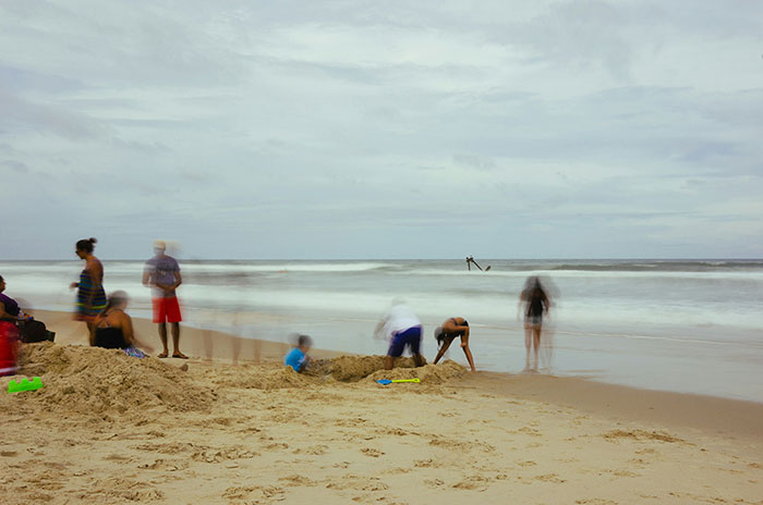 Blurry image of people at the beach with waves in the background.