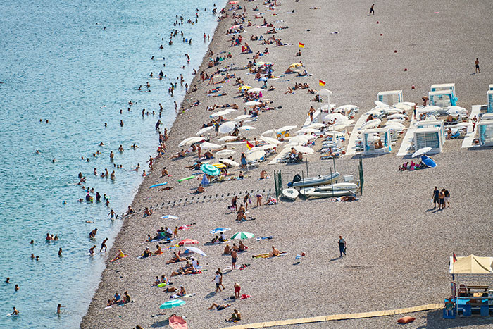 Crowded beach scene with people swimming and relaxing under umbrellas.