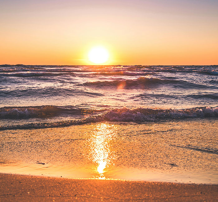 Sunset over ocean waves at the beach, golden light reflecting on the water.