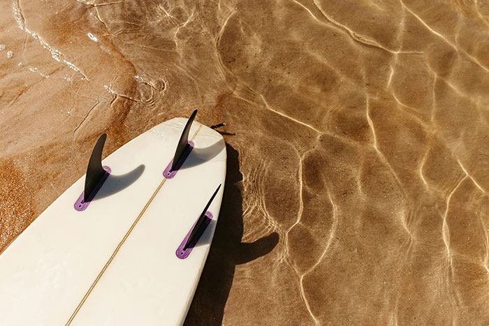 Surfboard on sandy beach with clear water ripples, capturing a serene moment at the beach.