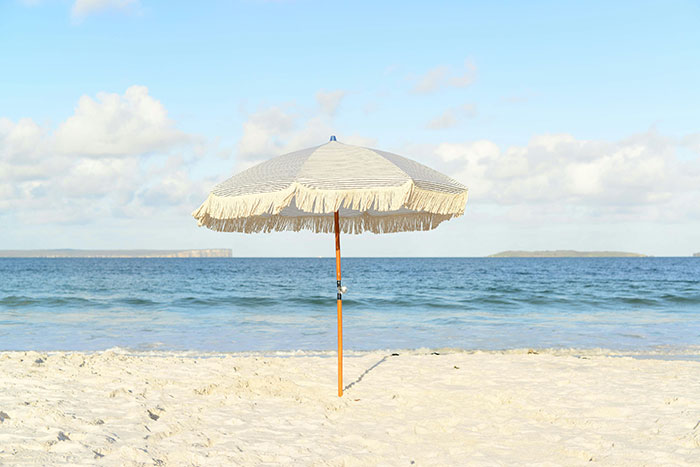 Beach scene with a single fringe umbrella on white sand under a clear sky.