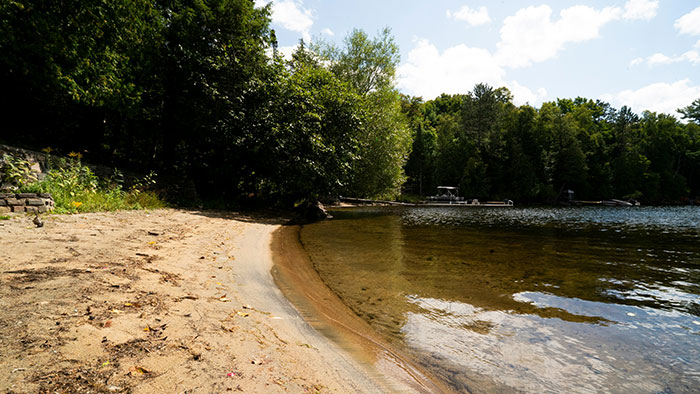A serene beach scene with clear water, trees, and a sandy shore under a partly cloudy sky.