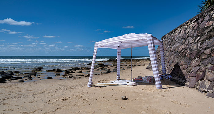 Beach scene with a white canopy, rocky shoreline, and clear blue sky.