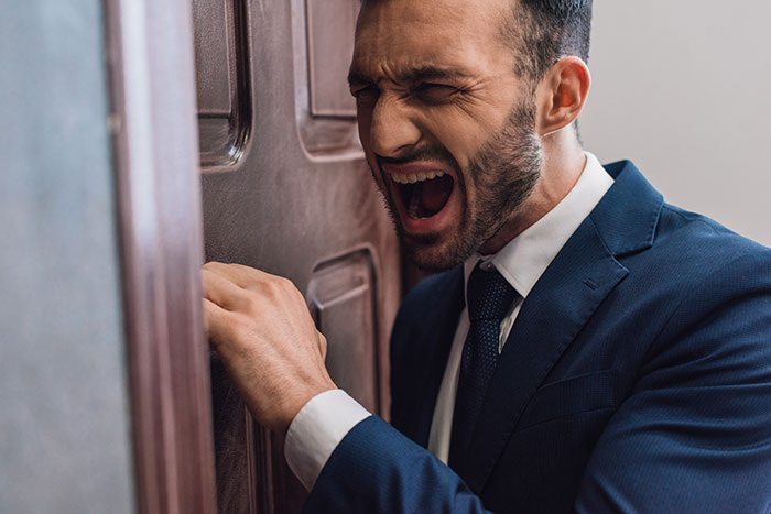 A man in a suit yelling at a wooden door, expressing frustration, related to tree cutting and petty revenge. A man in a suit yelling at a wooden door, expressing frustration, related to tree cutting and petty revenge.