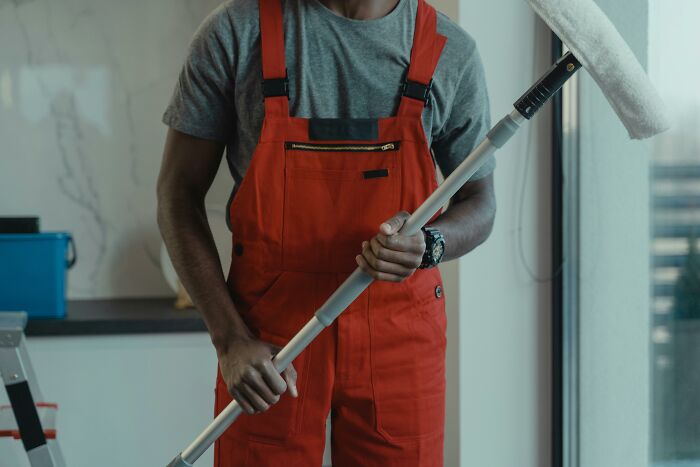 Person cleaning windows in red overalls, holding a squeegee indoors.