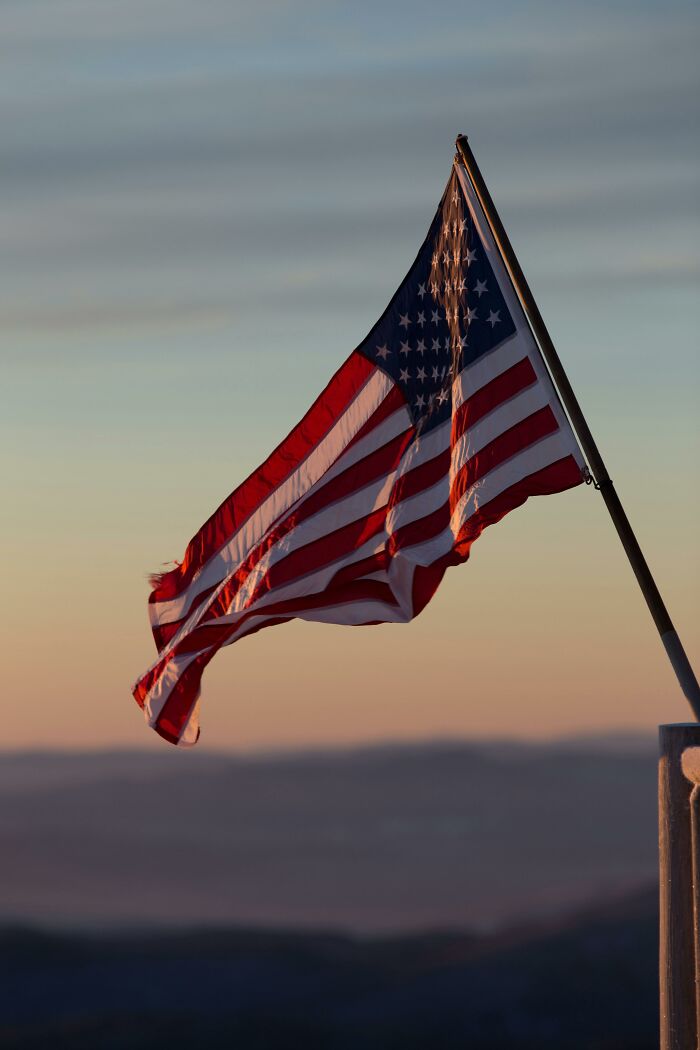 American flag waving at sunset, a symbol of current societal norms under discussion for future reflection.