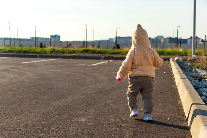 Toddler walks alone in an empty parking lot, highlighting child safety concerns.