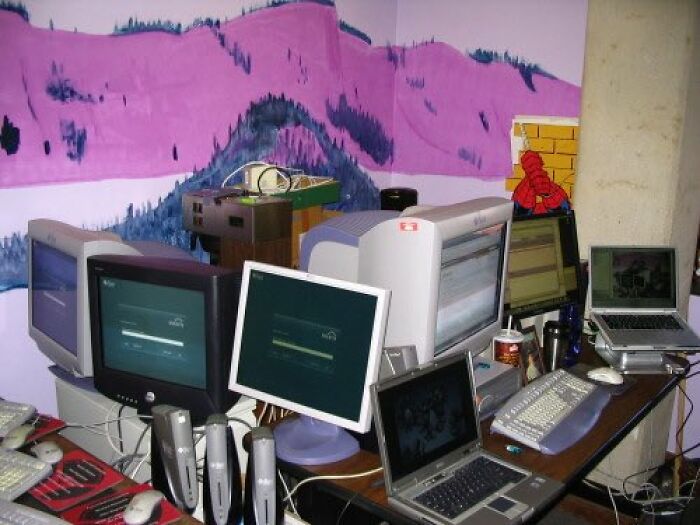 Old Internet feel with multiple vintage computer monitors and laptops on a cluttered desk, against a colorful wall mural.