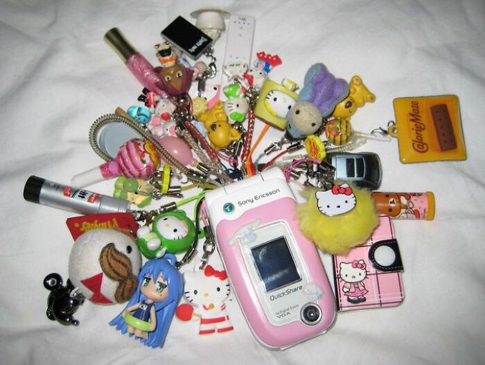 Old internet aesthetic with a Sony Ericsson phone and various colorful keychain charms.