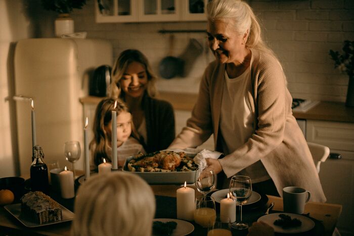 Elderly woman serving Christmas dinner to family, including children, in a warmly lit kitchen. Elderly woman serving Christmas dinner to family, including children, in a warmly lit kitchen.