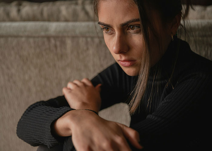 Pensive woman sitting on a sofa, arms crossed, contemplating relationship dynamics.
