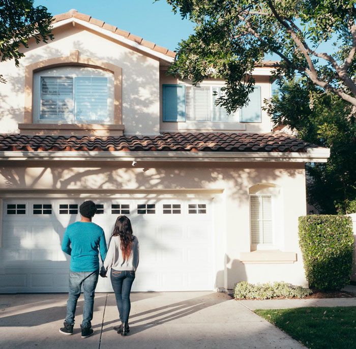 A couple stands in front of a suburban house under a clear sky, suggesting financial stability and family dynamics. A couple stands in front of a suburban house under a clear sky, suggesting financial stability and family dynamics.