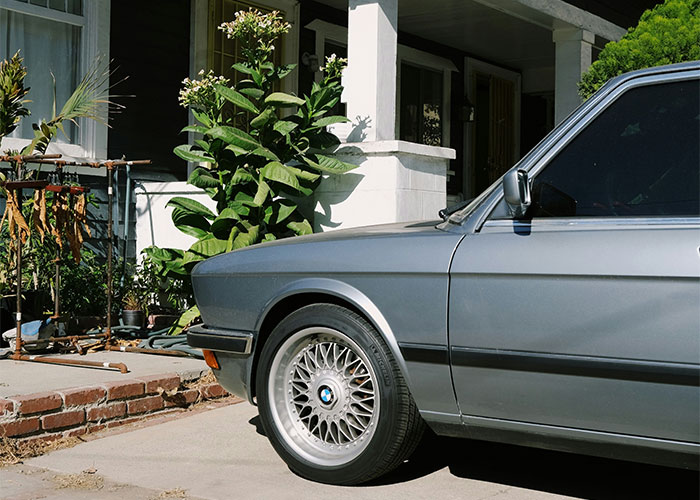 Car parked in a driveway next to a house with plants, emphasizing unauthorized parking consequences.