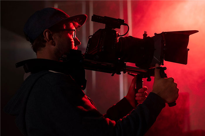 Person operating a camera with red lighting, revealing Hollywood secrets behind film production.