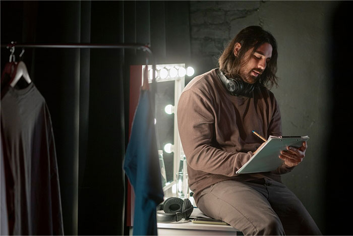 Person sitting in a dressing room, writing on a clipboard, capturing Hollywood secrets in a reflective, dimly lit setting.