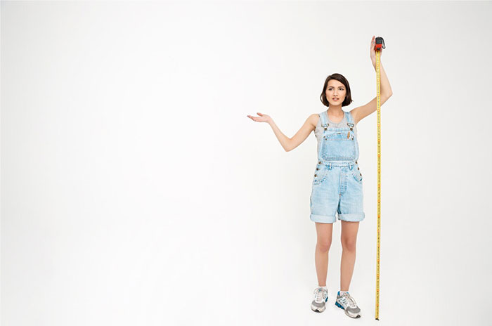 Person measuring height with tape, standing against a white background, symbolizing Hollywood secrets.