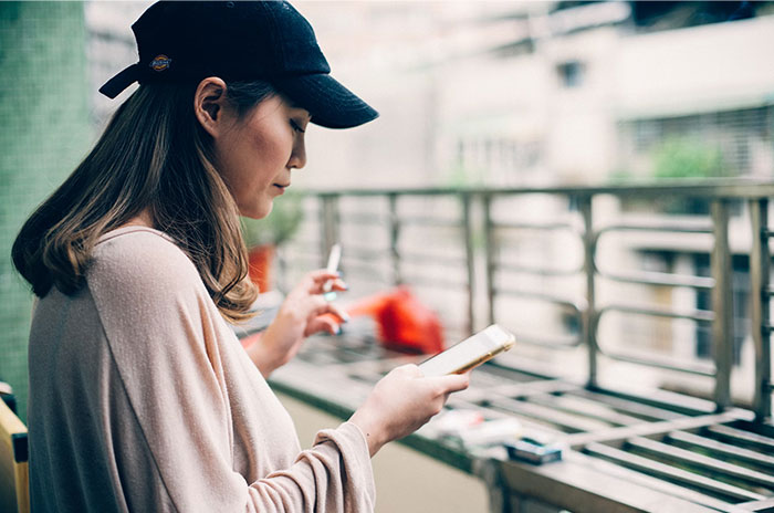 Woman on a balcony with a phone and cigarette, contemplating Hollywood secrets.