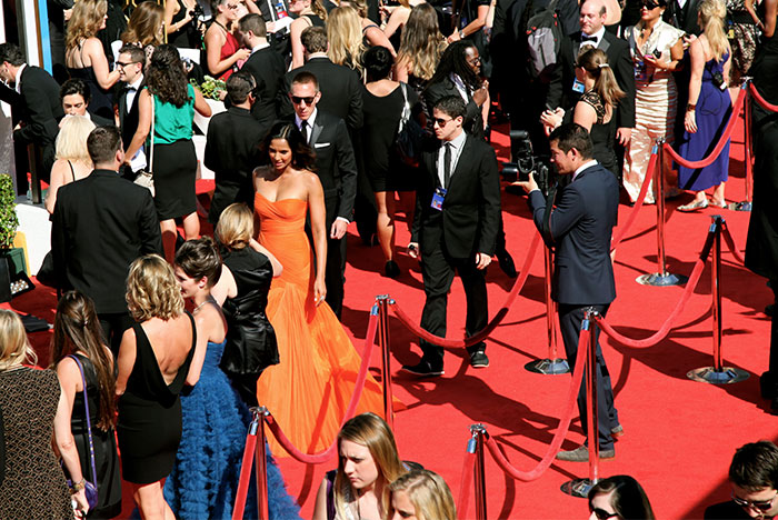 People sharing Hollywood secrets on a bustling red carpet event filled with elegantly dressed attendees.