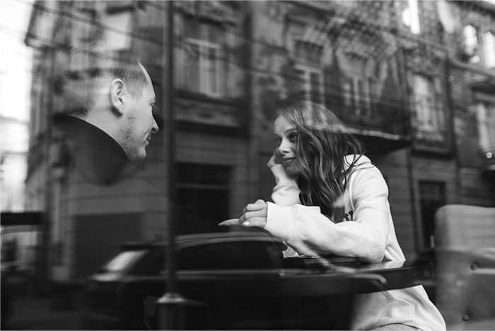 Two people sitting at a cafe table behind glass, sharing secrets in Hollywood.