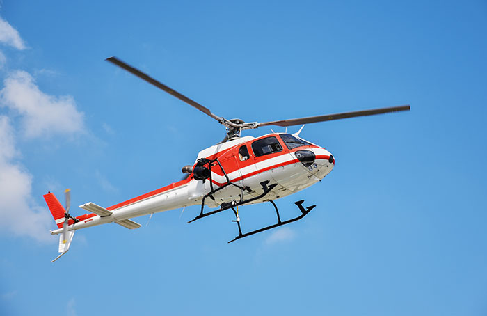 Red and white helicopter flying in a clear blue sky, representing jobs with little work required.
