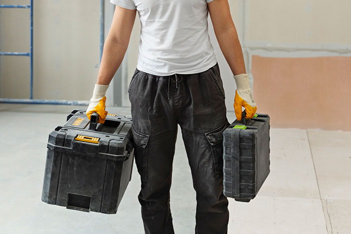Person in casual work attire holding two toolboxes, representing easy jobs with minimal effort.