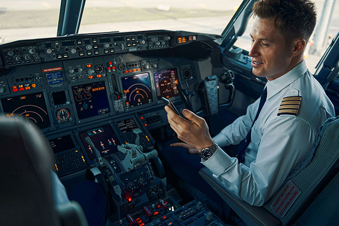Pilot in the cockpit using a smartphone, illustrating jobs with minimal work responsibilities.