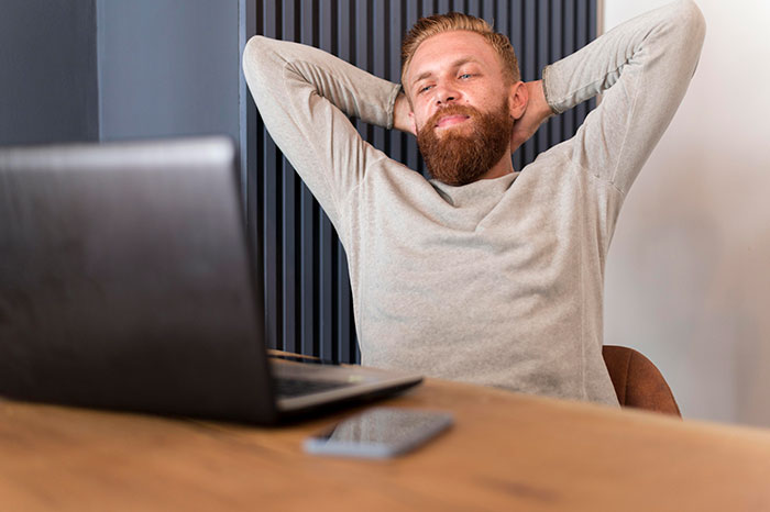 Man relaxing at a desk with a laptop, representing jobs with minimal work and easy money.