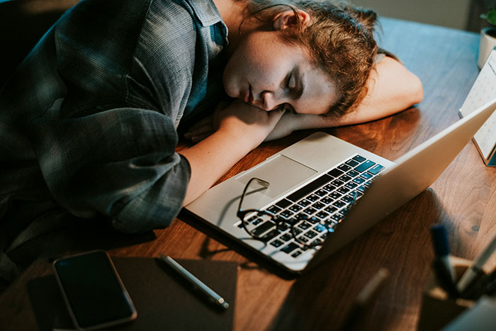 Person napping on a desk beside a laptop, representing easy jobs with minimal work effort.