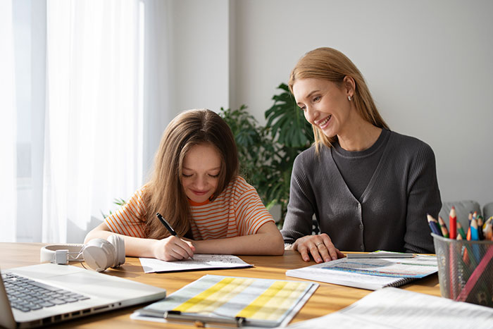 Woman overseeing a girl's homework at a desk, illustrating a low-effort job scenario.