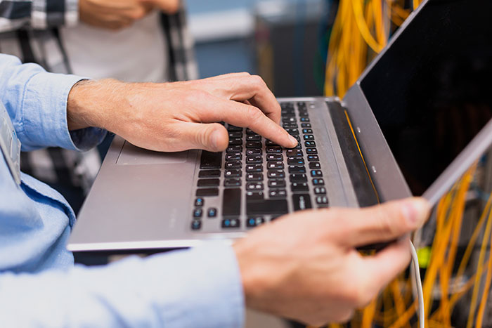 Person holding a laptop with one hand, typing with the other, representing minimal work effort in tech jobs.