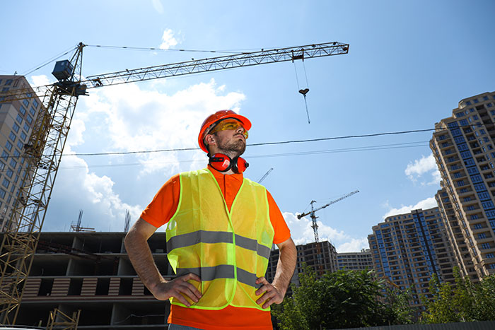 Construction worker in safety gear at a building site with cranes and skyscrapers in the background.