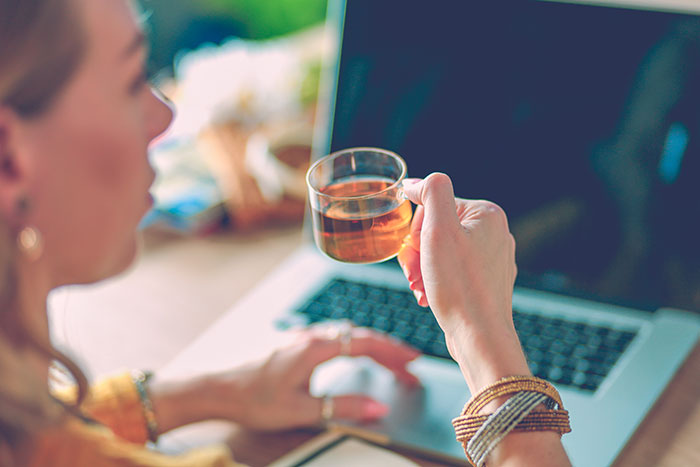 Person holding tea, sitting at a laptop, illustrating a job where people are paid for minimal work.