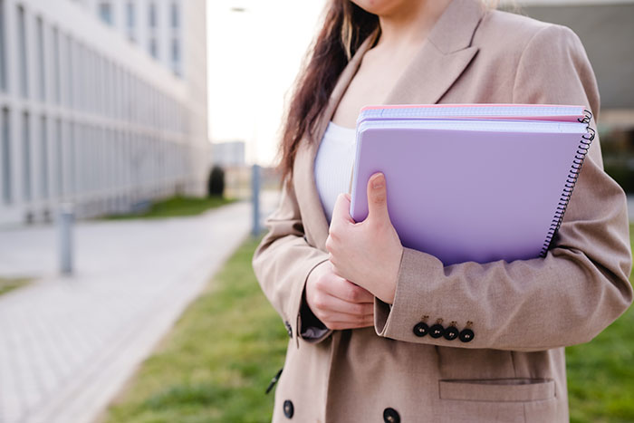 Woman in a tan blazer holding notebooks, symbolizing easy jobs with minimal work effort.