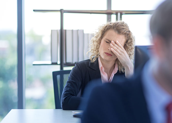 A woman in an office covering her face in embarrassment, reflecting on a painfully embarrassing moment.