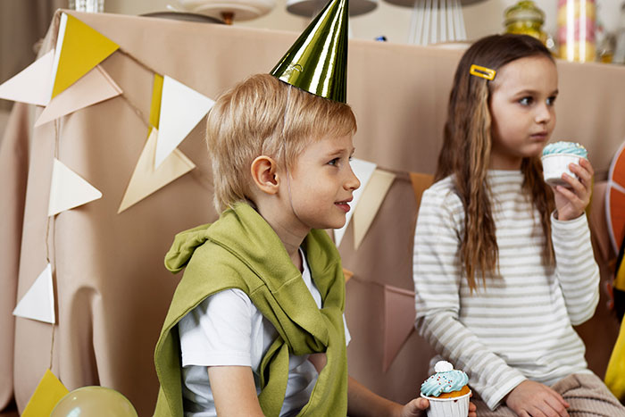 Children at a party, wearing hats and holding cupcakes, embodying embarrassing moments.