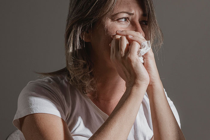 A woman in a white shirt looking distressed, covering her mouth with her hand, conveys a painfully embarrassing moment.