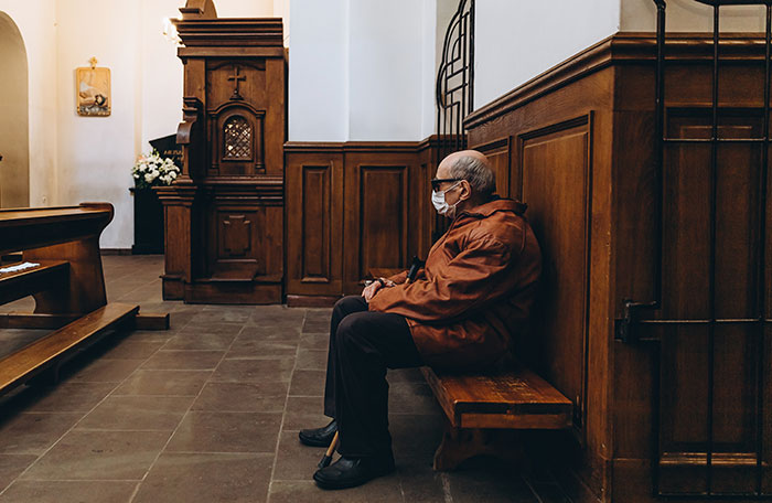 A person sitting in a church pew, wearing a mask, contemplating embarrassing moments.