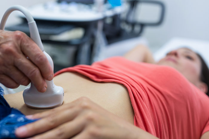 Ultrasound scan in progress; a patient in a coral shirt receives an abdominal examination.