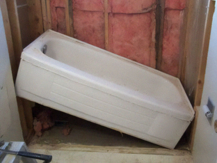 Unevenly installed bathtub surrounded by exposed insulation, showcasing nothing interesting.