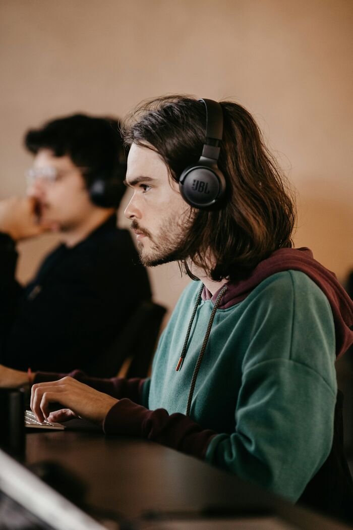 Person with long hair and headphones, focused on a computer, illustrating cringe moments.