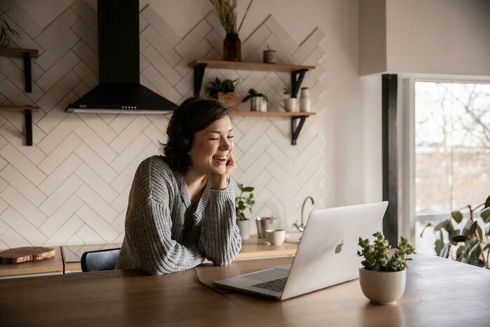 Person smiling at a laptop in a cozy kitchen, embodying a moment of cringe.