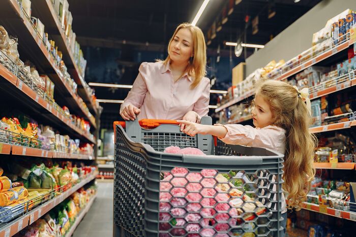 Mother and daughter shopping, reaching new heights of cringe with puzzled expressions in a grocery aisle.