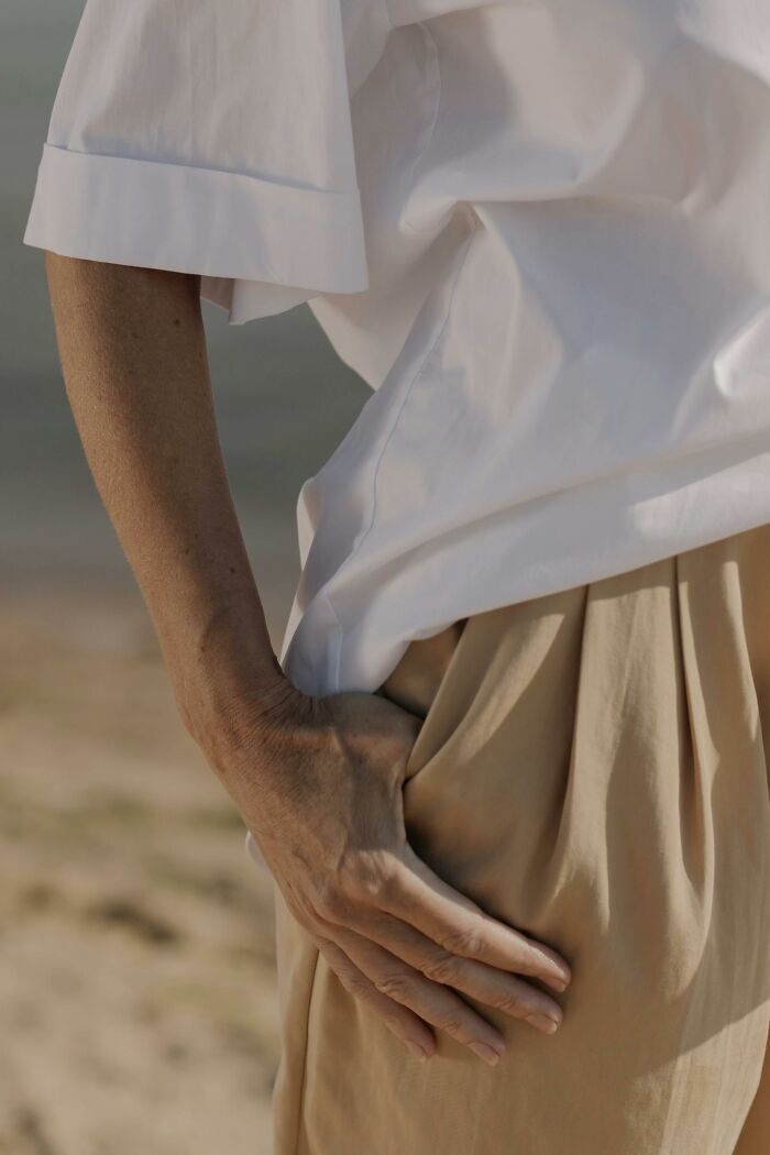 A person wearing a white shirt and beige pants stands with a hand in the pocket, capturing a moment of cringe.