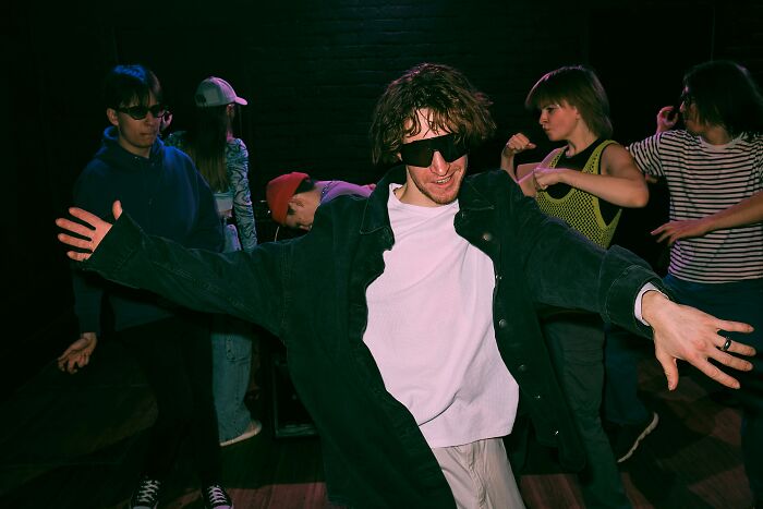 Person wearing sunglasses dancing awkwardly with friends in a dimly lit room, capturing a moment of cringe.