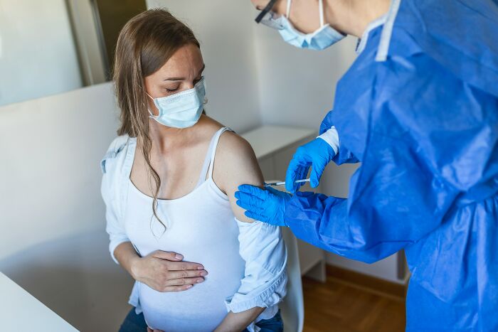 A pregnant woman receives a vaccine from a healthcare worker in protective gear.
