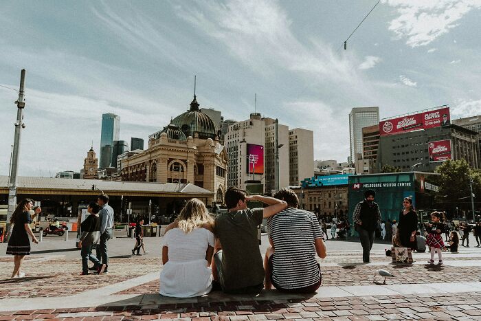 Three friends sitting together, overlooking a busy city square, symbolizing friendships turned strangers.