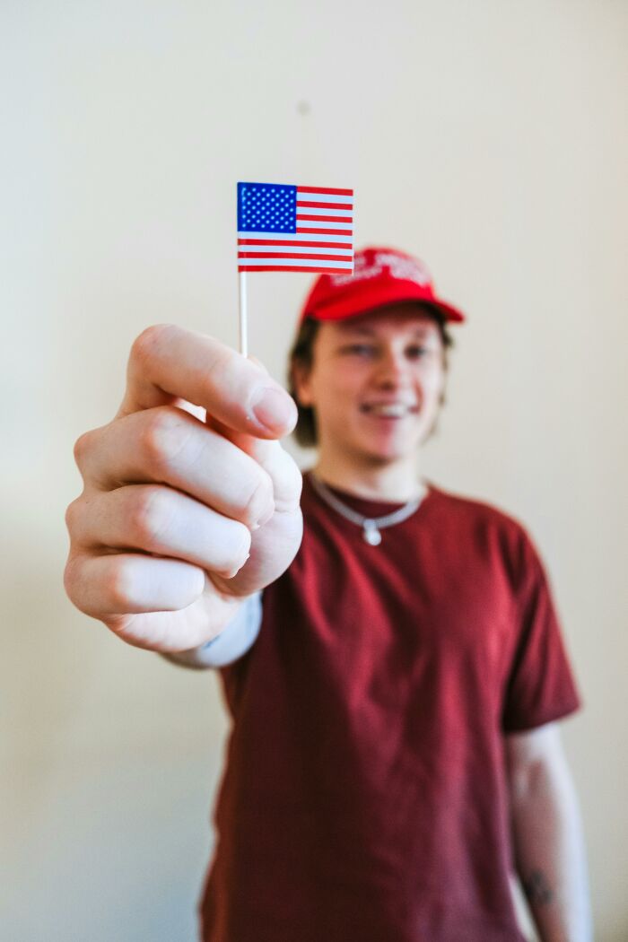 Person in a red shirt and cap holding a small American flag, symbolizing distance or change in friendships.