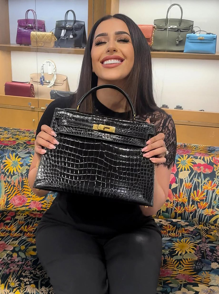 Dubai housewife Linda Andrade holding a luxury handbag in front of a display of designer bags.
