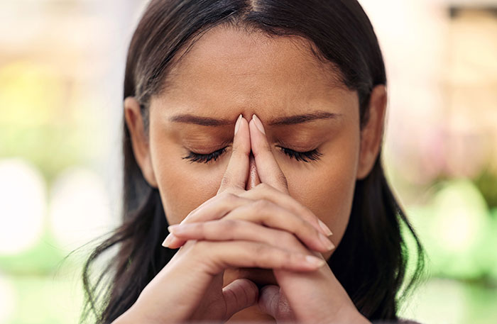 A person contemplating with closed eyes, hands pressed together, reflecting on wedding gift expectations.